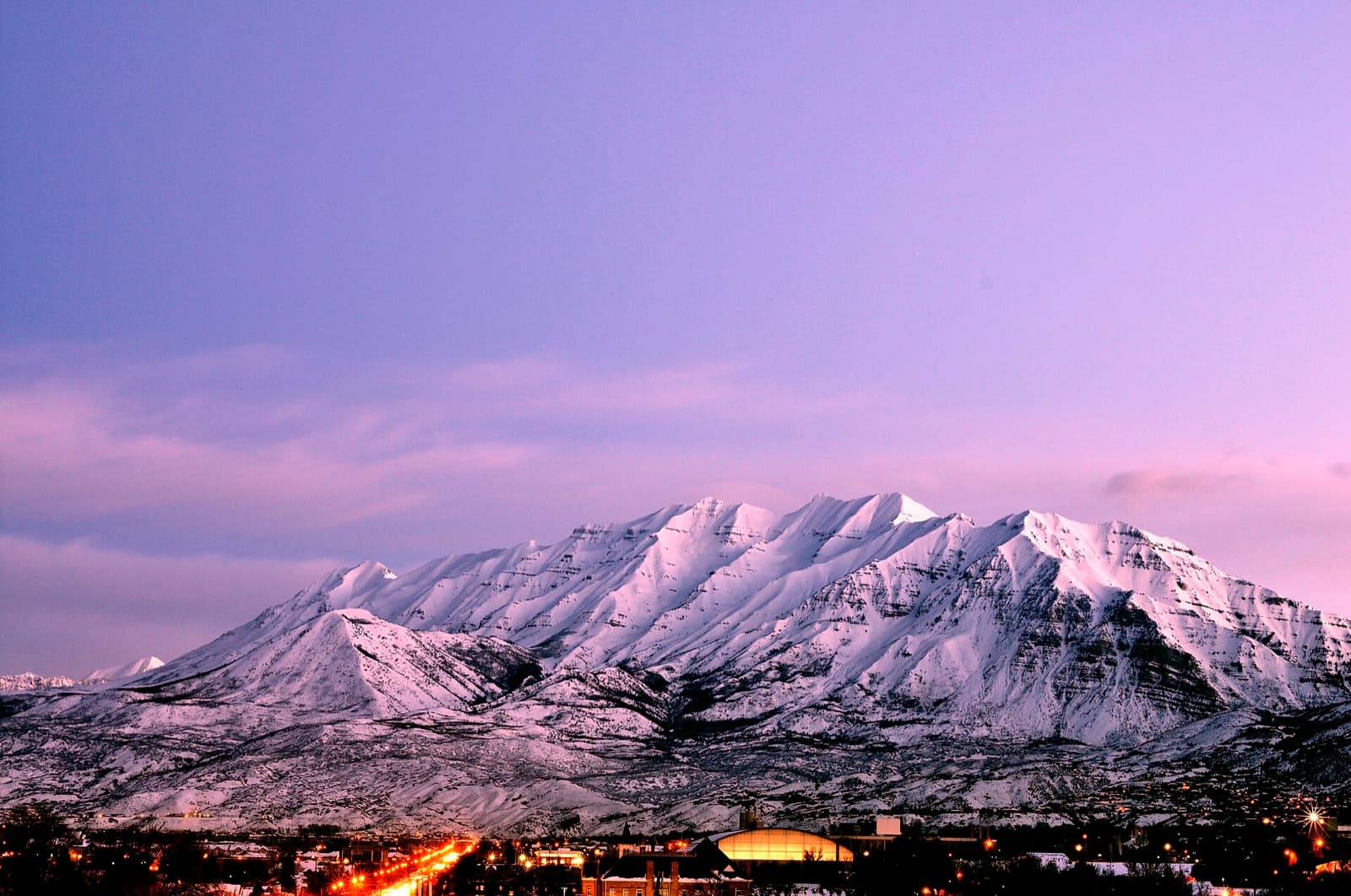 Snow on Mount Timpanogos at dusk, above the lights of a Utah Valley town